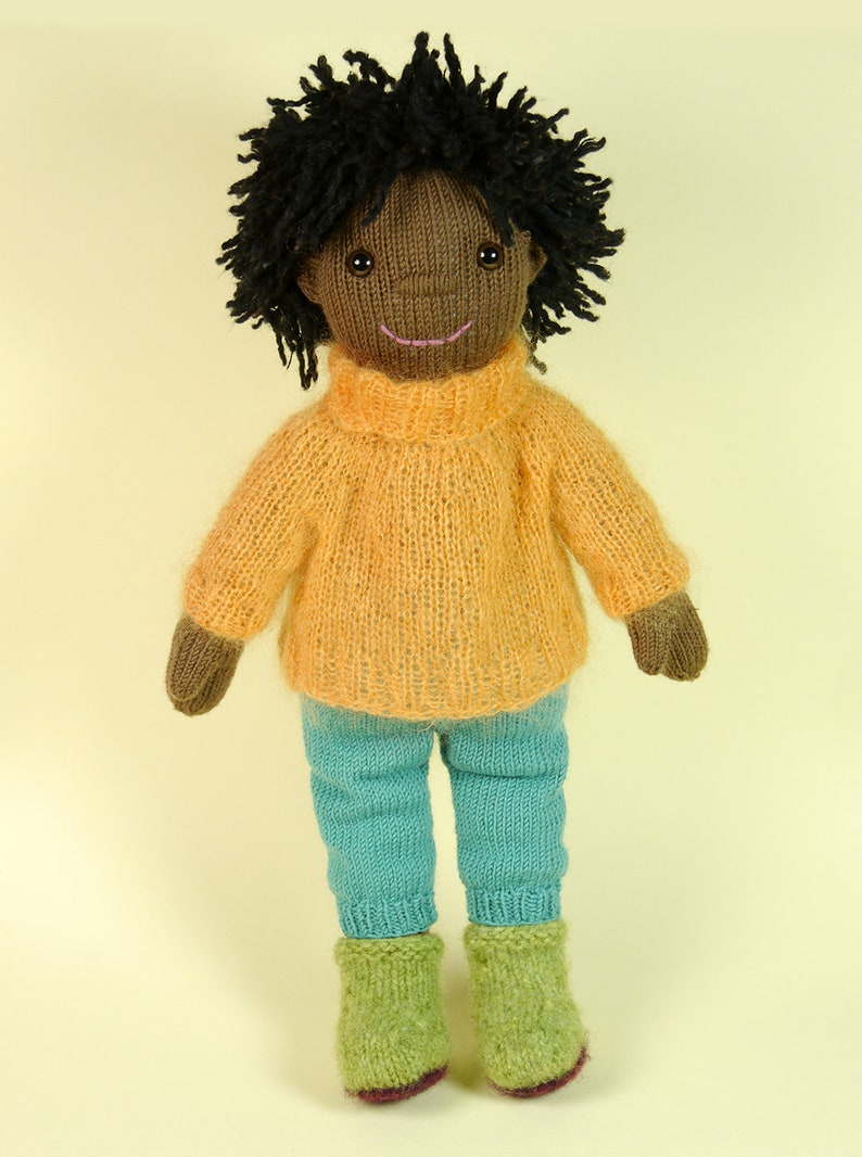 May include: A knitted doll with brown skin, black curly hair, a yellow sweater, blue pants, and green boots.