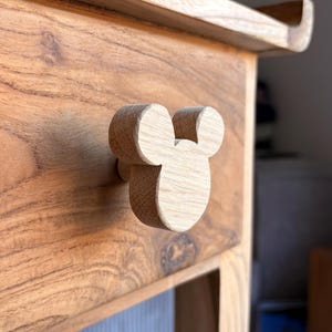 Könnte beinhalten: Holzschubladengriff in Form eines Mäusekopfes, befestigt an einer Holzschublade. Der Knopf ist hellbraun und die Schublade ist dunkler braun. Die Schublade ist Teil eines Holzschranks oder -tisches.