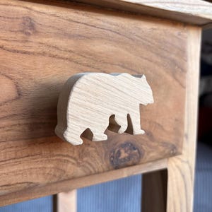Könnte beinhalten: Holzschublade mit einem Griff in Form eines Bären aus hellem Holz. Der Bär ist mit einem einfachen Design geschnitzt. Das Holz der Schublade und des Möbels hat eine warme, natürliche Oberfläche.