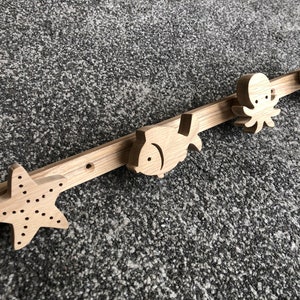 Può includere: Appendiabiti da parete in legno chiaro con creature marine. Presenta una stella marina, un pesce, un polpo e un cavalluccio marino. Ideale per una camera a tema marino o per decorazioni nautiche.