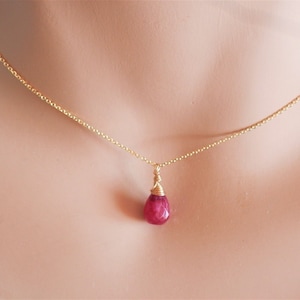 May include: A gold chain necklace with a single teardrop-shaped ruby pendant.