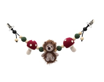 May include: A crocheted baby toy with a hedgehog, mushrooms, and wooden beads. The toy has two clips for attaching to a stroller or crib.