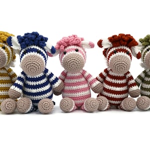 Op de afbeelding: Vijf handgemaakte gehaakte zebrapoppen in verschillende kleuren. Elke zebra heeft een andere gekleurde manen en gestreept lichaam. Kleuren zijn goud, blauw, roze, rood en groen. De poppen zitten rechtop met hun benen uitgestrekt.