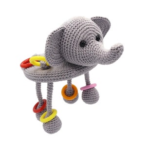 May include: A gray crocheted elephant toy with colorful rings attached to its legs. The elephant has a long trunk and large ears.