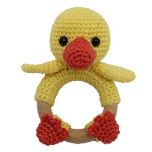 May include: A yellow crocheted duck rattle with a wooden ring and red crocheted feet.