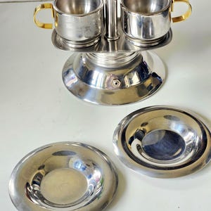 Op de afbeelding: Een set van drie keramische mokken met een gespikkelde, matte afwerking. De mokken zijn in de kleuren crème, lichtgrijs en donkergrijs. Elke mok heeft een eenvoudig, minimalistisch ontwerp en een afgeronde handgreep.