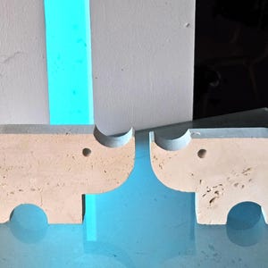 May include: Two white ceramic elephant figurines facing each other. The elephants are simple and abstract in design, with no details other than their trunks and ears.
