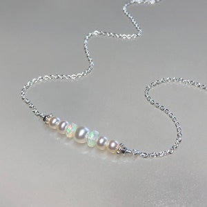 May include: A delicate silver chain necklace with a row of white pearls and opals.