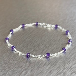 May include: A delicate silver chain bracelet with small purple amethyst beads. The bracelet is made of sterling silver and features a lobster clasp closure.