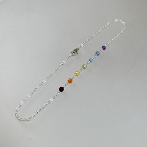 May include: A silver chain anklet with seven small round gemstones in rainbow colours. The gemstones are red, orange, yellow, green, blue, light blue, and purple.