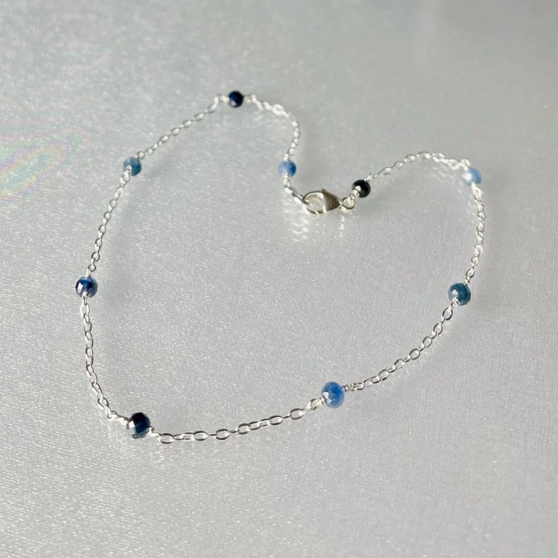 Peut inclure: Un bracelet de cheville fin en argent avec de petites perles de pierres pr&eacute;cieuses bleues.