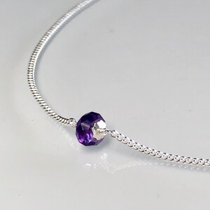 May include: A delicate silver chain necklace with a single, faceted amethyst gemstone pendant.