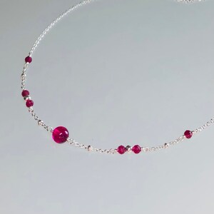 May include: A silver chain necklace with small red gemstone beads and a larger red gemstone pendant.