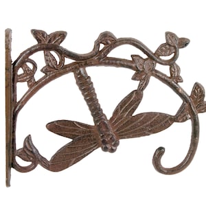 Könnte beinhalten: Ein Wandhaken aus Gusseisen in Form einer Libelle mit einem Blatt-Ranken-Design. Der Haken ist in einem rustikalen Braunton lackiert.