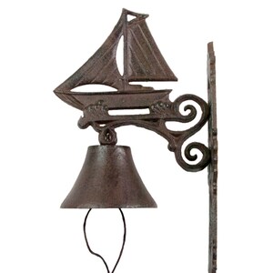 May include: A cast iron door bell with a sailboat design and a bell with a rope pull. The bell is brown and has a rustic finish.