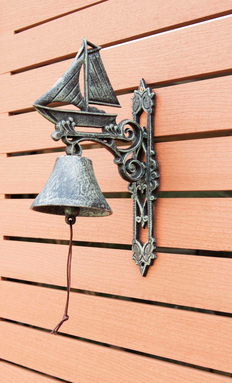 May include: A black cast iron door knocker with a sailboat design and a bell. The knocker is mounted on a wooden door.