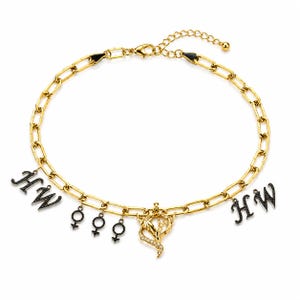 May include: A gold-tone chain necklace featuring a lobster clasp and an extender. The necklace is adorned with two black letter charms reading HW, three black gender symbol charms, and a central gold-tone pendant with clear stones.