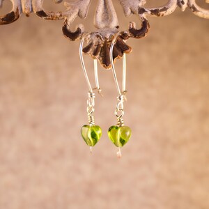 Op de afbeelding: Een paar zilveren oorhangers met groene glazen hartvormige kralen.