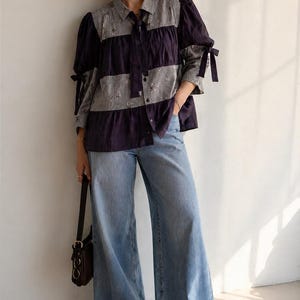 May include: A navy and white striped blouse with a bow and puffed sleeves, worn with light wash wide-leg jeans. A black handbag is carried over the shoulder. The outfit is casual.