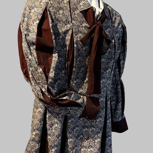 Peut inclure: Une chemise à motifs avec un nœud papillon marron foncé. La chemise présente un motif circulaire répétitif dans les tons marron, blanc et gris. Le tissu marron foncé accentue les manches et les panneaux avant. La chemise est présentée sur un mannequin.