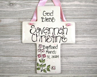 May include: White ceramic cross with pink polka dots. The cross has the text "God Bless Savannah Christine" and "Baptized March 31, 2024" with a floral design.