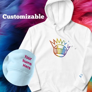 Könnte beinhalten: Weißer Hoodie mit einem regenbogenfarbenen Grafikdruck eines Cartoon-Gesichts mit einer Krone. Der Hoodie hat eine Kapuze und eine Kängurutasche. Der Text "Customizable" befindet sich in der oberen linken Ecke des Bildes. Ein hellblauer Hut mit dem Text "Your Name Here" befindet sich in der unteren linken Ecke des Bildes.