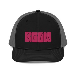 May include: A black and gray trucker hat with a pink "KCLU" logo embroidered on the front.