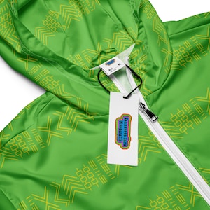 Könnte beinhalten: Grüne Kapuzenjacke mit einem weißen Reißverschluss und einem gelben geometrischen Muster. Die Jacke hat ein Etikett mit der Aufschrift "Funness & Woodcrafts".