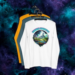 May include: White long-sleeve t-shirt with a colorful graphic of a landscape with mountains, a river, and a moon. The graphic is in a circle with the text "COSMIC COUNTRY" around it.