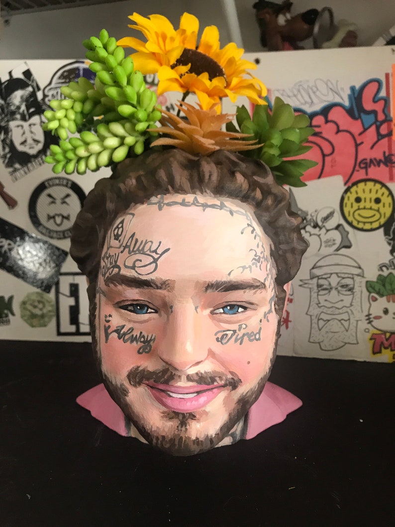 May include: A ceramic head planter featuring a painted portrait with tattoos and a beard. The planter is adorned with artificial sunflowers and succulents. The face has the words "Stay Away" and "Tired" tattooed on it.