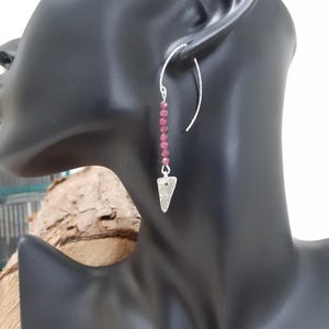 May include: Silver dangle earrings with a triangle charm and a row of small, dark pink beads.