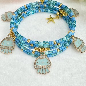 May include: A multi-strand bracelet made of blue and gold beads with four dangling charms shaped like jellyfish. The charms are light blue with gold accents.