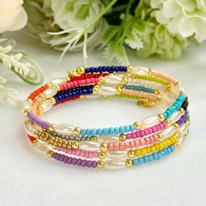 Könnte beinhalten: Mehrfarbiges Perlenarmband mit weißen Perlenakzenten. Das Armband besteht aus kleinen, bunten Perlen und hat ein mehrschichtiges Design.