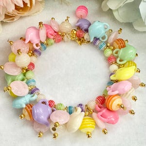 以下が含まれることがあります： 様々な形と色を持つカラフルなビーズブレスレット。ピンク、黄色、青などのパステルカラーのティーポット、球体、その他の形のビーズが含まれています。ブレスレットはゴールドチェーンに通されています。