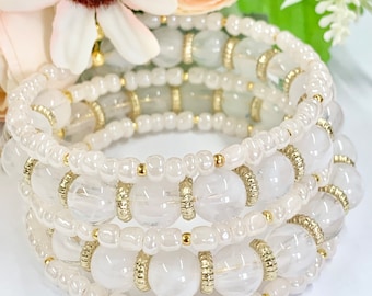 Puede incluir: Un brazalete de múltiples hilos con cuentas de cuarzo transparente con detalles dorados. El brazalete está hecho de varias capas de cuentas, creando un aspecto en capas y texturizado.