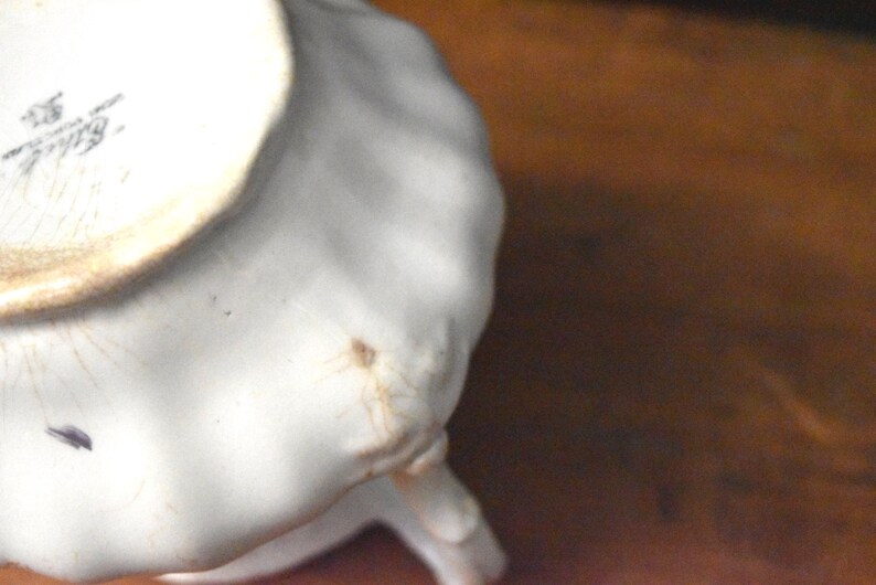 May include: Close-up of a white ceramic object with a scalloped edge. The object has a slightly textured surface and a small, dark spot. The underside shows a partial view of a stamp.