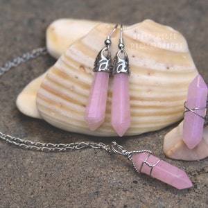 Könnte beinhalten: Ein Set aus rosafarbenem Kristallschmuck mit einer Halskette, Ohrringen und einem Ring. Die Halskette und die Ohrringe haben silberne Ketten- und Drahtakzente. Der Ring ist aus einem silbernen Band und Draht gefertigt, der um den Kristall gewickelt ist.