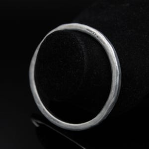 May include: A circular silver bangle bracelet with a matte, hammered texture and an irregular, organic shape. The metal surface displays subtle indentations and a soft, non-reflective finish. The word "A.Kramer" is engraved on the inner band surface.