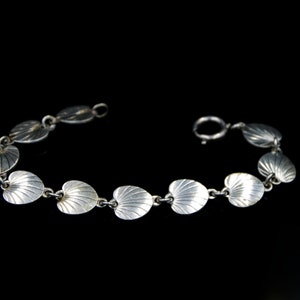 May include: A silver bracelet with a chain made of small, connected heart-shaped links. Each heart has a textured, ridged surface.
