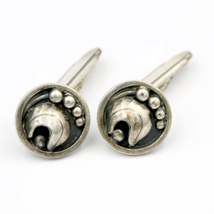 May include: A pair of silver cufflinks featuring a stylised design of a helmet with a black background and silver accents.