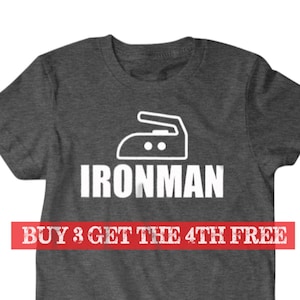 Puede incluir: Una camiseta gris oscuro con un icono de plancha blanco y el texto "IRONMAN" impreso en la parte delantera. El texto "BUY 3 GET THE 4TH FREE" est&aacute; impreso en rojo debajo del dise&ntilde;o.