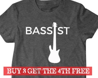 May include: A dark heather grey t-shirt with the word "BASSIST" printed in white, and a white silhouette of a bass guitar. The text "BUY 3 GET THE 4TH FREE" is printed in red at the bottom of the shirt.