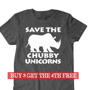 Puede incluir: Una camiseta gris oscuro jaspeada con una silueta blanca de un rinoceronte y el texto "Save the Chubby Unicorns". El texto "Buy 3 Get the 4th Free" está impreso en rojo en la parte inferior de la camiseta.