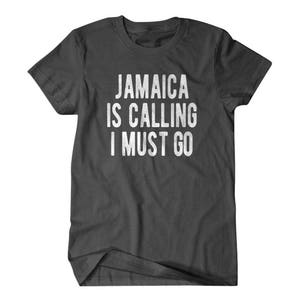 Pu&ograve; includere: Una maglietta grigia scura con il testo "Jamaica is calling I must go" stampato in bianco.