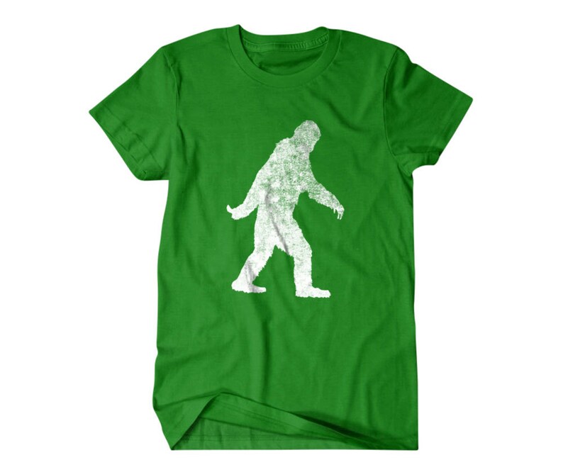 Puede incluir: Camiseta verde con una silueta blanca de Bigfoot caminando.