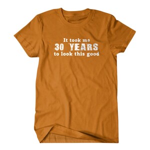 May include: A mustard yellow t-shirt with the text "It took me 30 YEARS to look this good" printed in white.