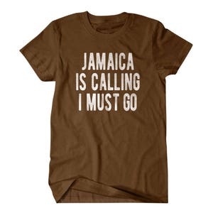 Pu&ograve; includere: Maglietta marrone con testo bianco che dice "Jamaica is calling I must go".
