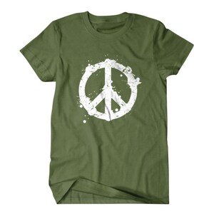 Puede incluir: Una camiseta verde con un gr&aacute;fico de signo de paz blanco. El signo de paz est&aacute; estilizado con un efecto de pintura salpicada.