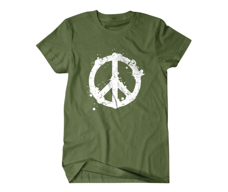 Puede incluir: Una camiseta verde con un gr&aacute;fico de signo de paz blanco. El signo de paz est&aacute; estilizado con un efecto de pintura salpicada.