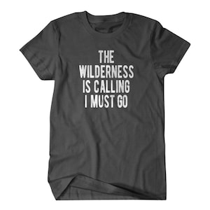 May include: A dark gray t-shirt with white text that reads "The Wilderness Is Calling I Must Go".